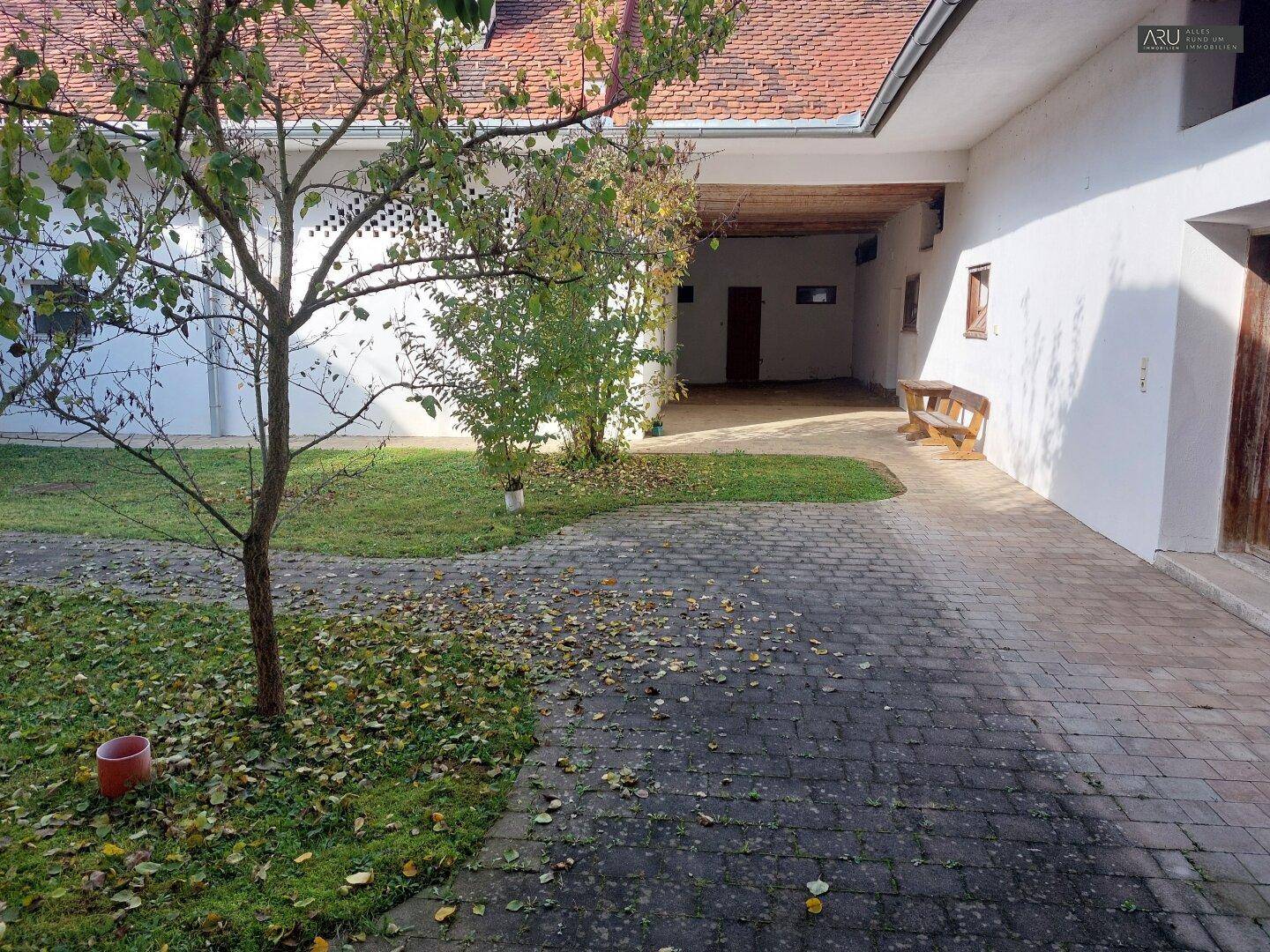 Sonniger Innenhof mit gepflastertem Bereich, Rasenflächen und jungen Bäumen, umgeben von Gebäuden.
