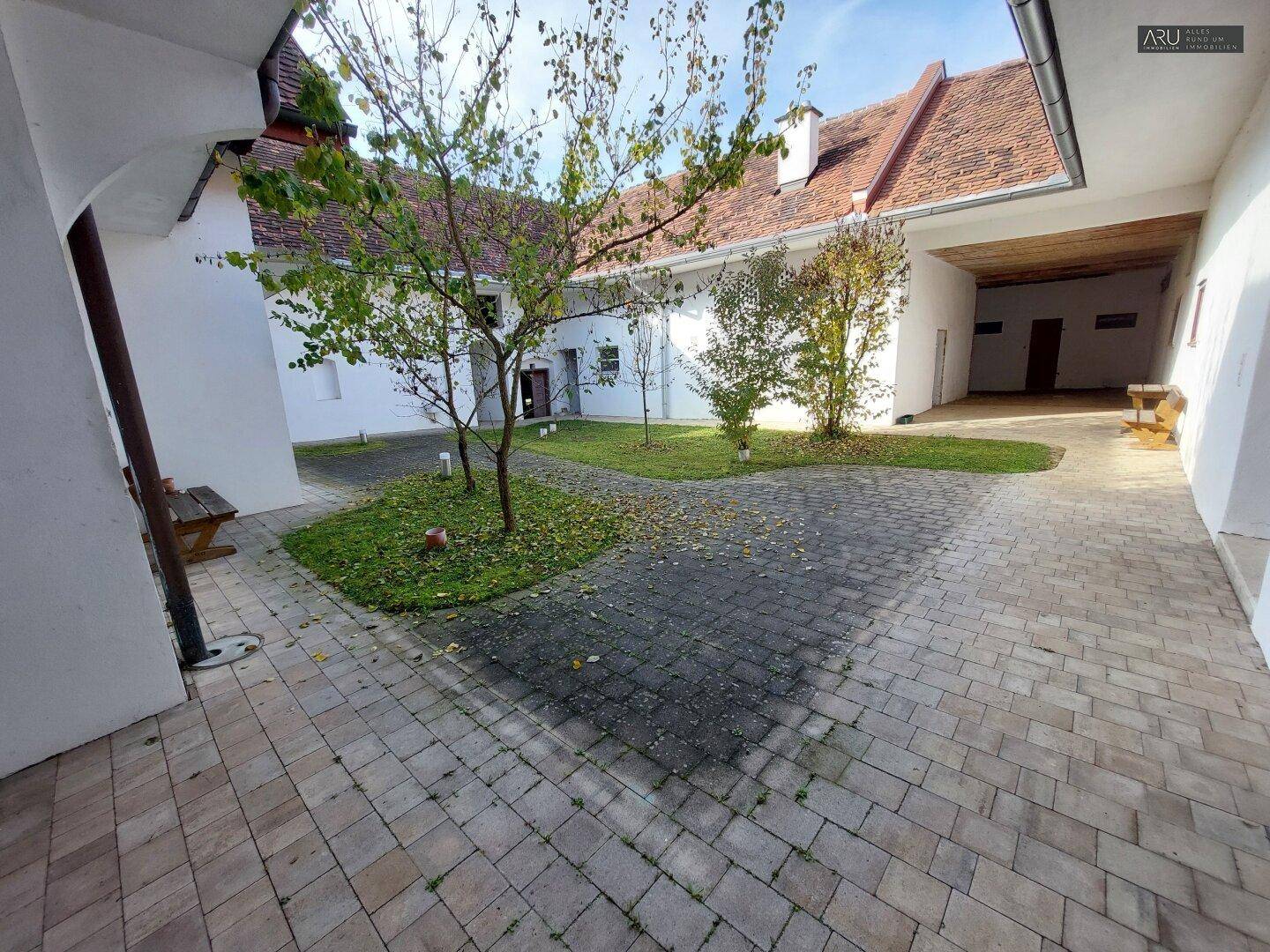 Gepflasterter Innenhof mit kleinen Bäumen und Grünflächen, umgeben von den Gebäudeteilen des Anwesens.