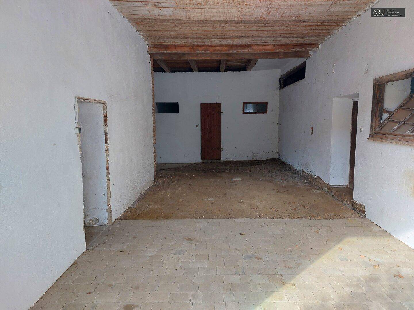 Großer, unausgebauter Raum mit Holzbalkendecke und einfachen Wänden, möglicherweise eine Scheune oder Garage.