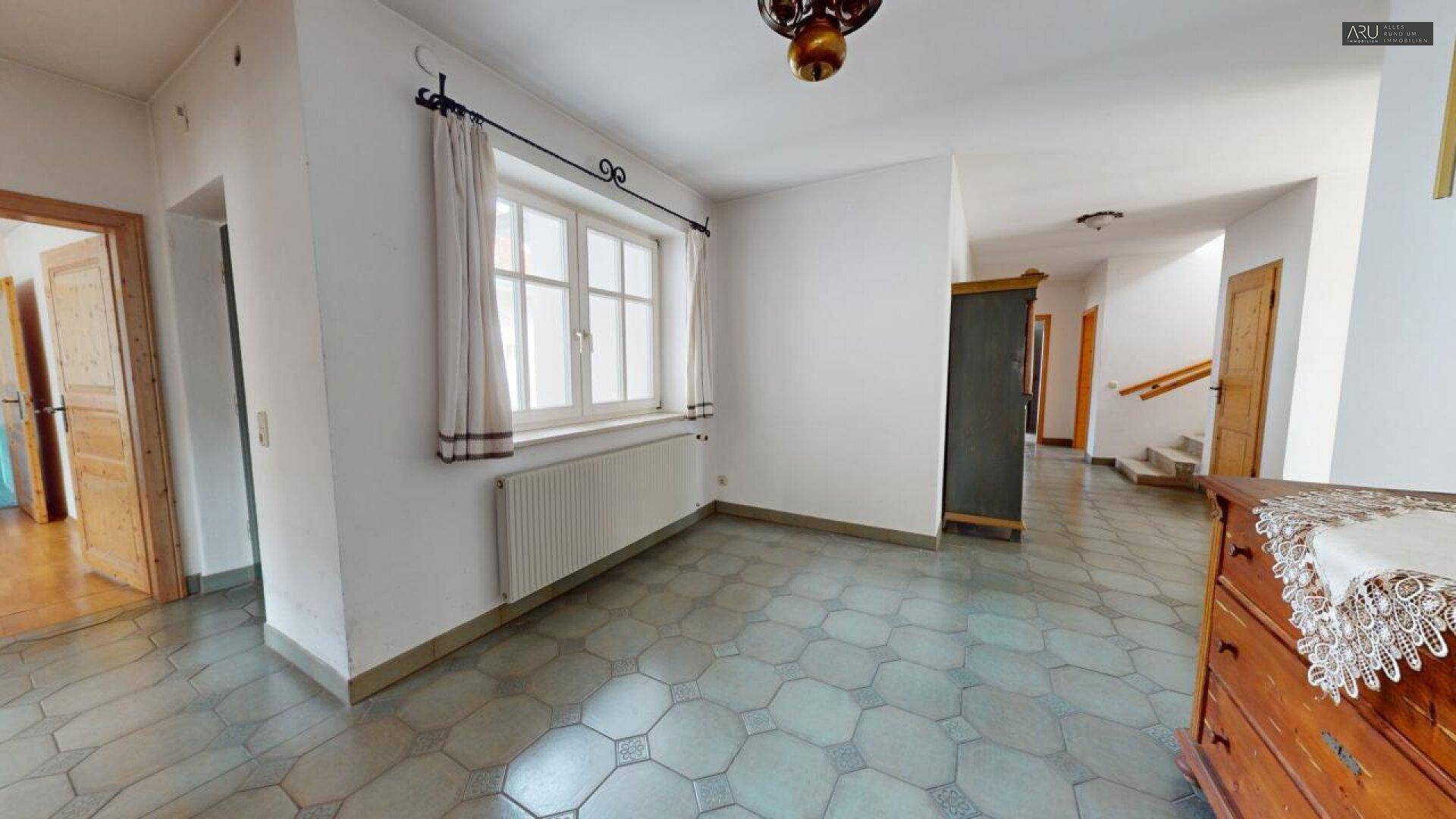 Geräumiger Flur mit Fliesenboden, einem Fenster und einem traditionellen Holzschrank.