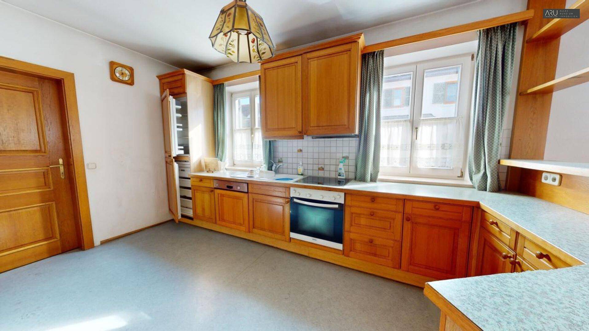 Traditionelle Holzküche mit Einbauschränken, Herd und Spüle unter zwei Fenstern.