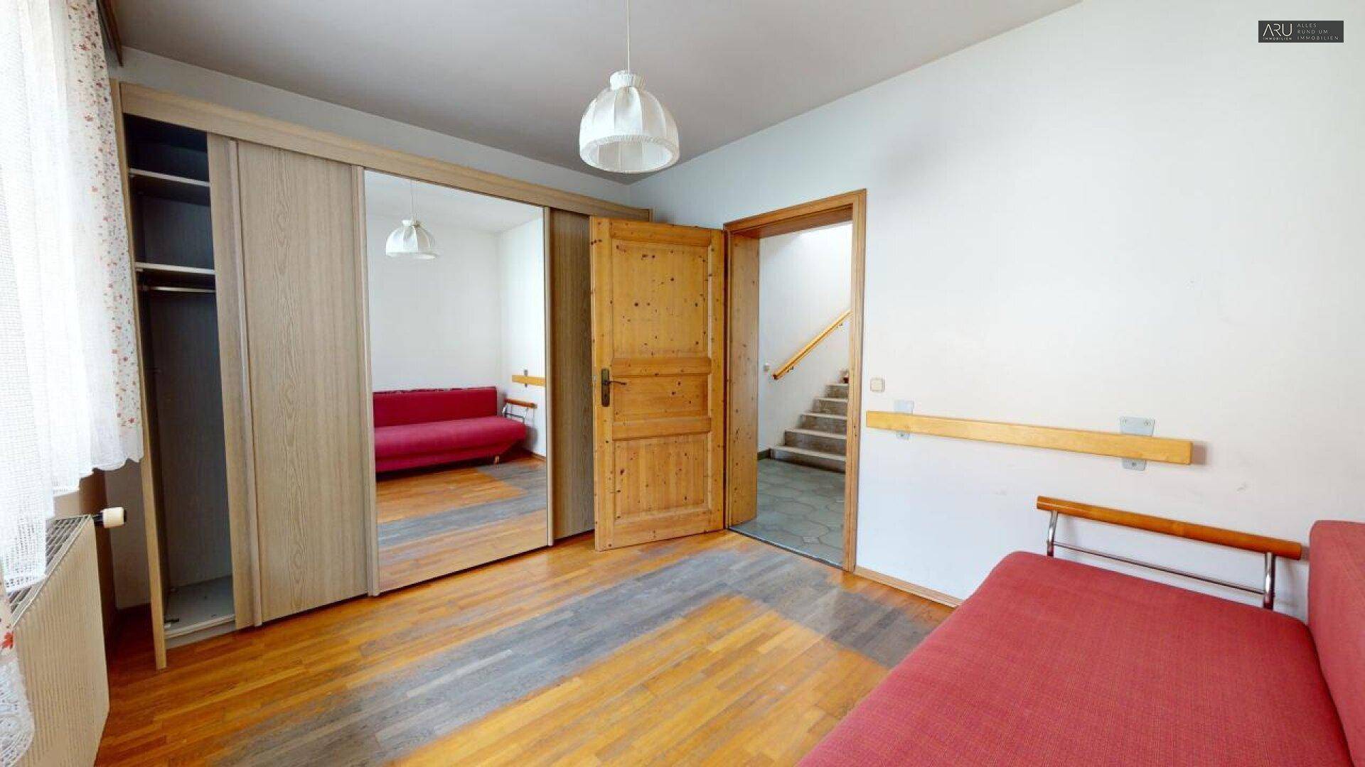 Helles Zimmer mit Holzboden, Einbauschrank und Zugang zu einem Treppenhaus.