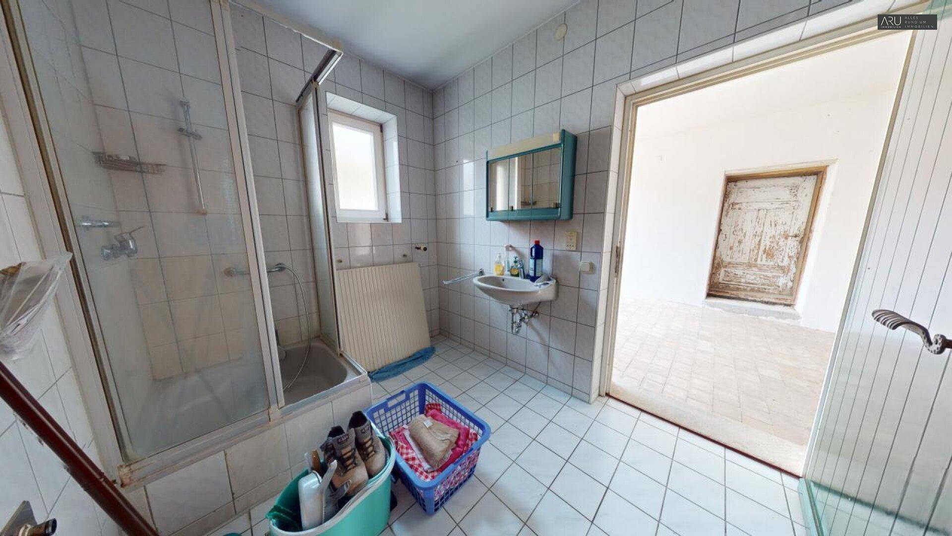 Badezimmer mit Duschkabine, Waschbecken und Fenster, ausgestattet mit einfachen Fliesen.