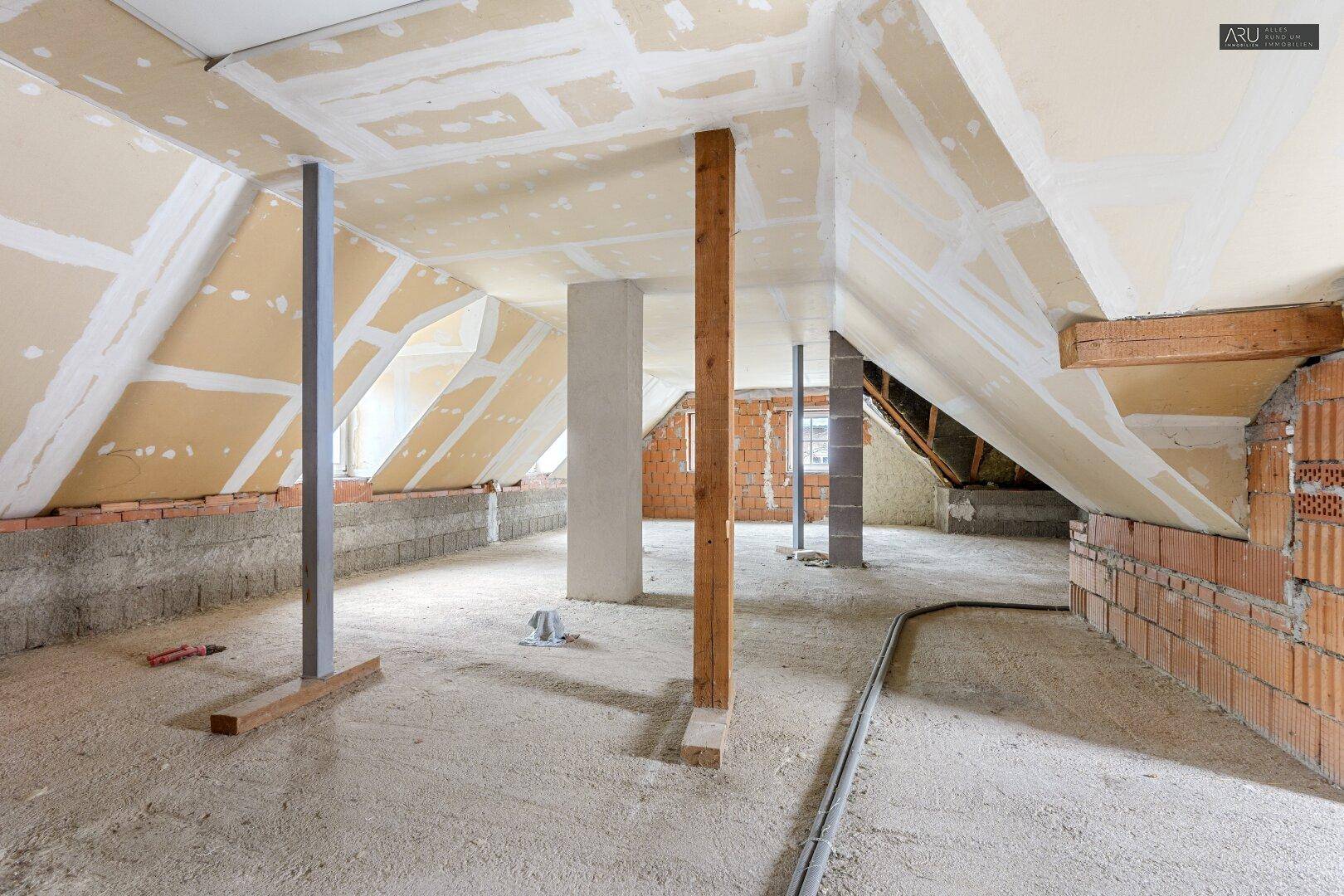 Unausgebauter Dachbodenbereich mit sichtbaren Dachschrägen, Ziegelwänden und Stützpfeilern.