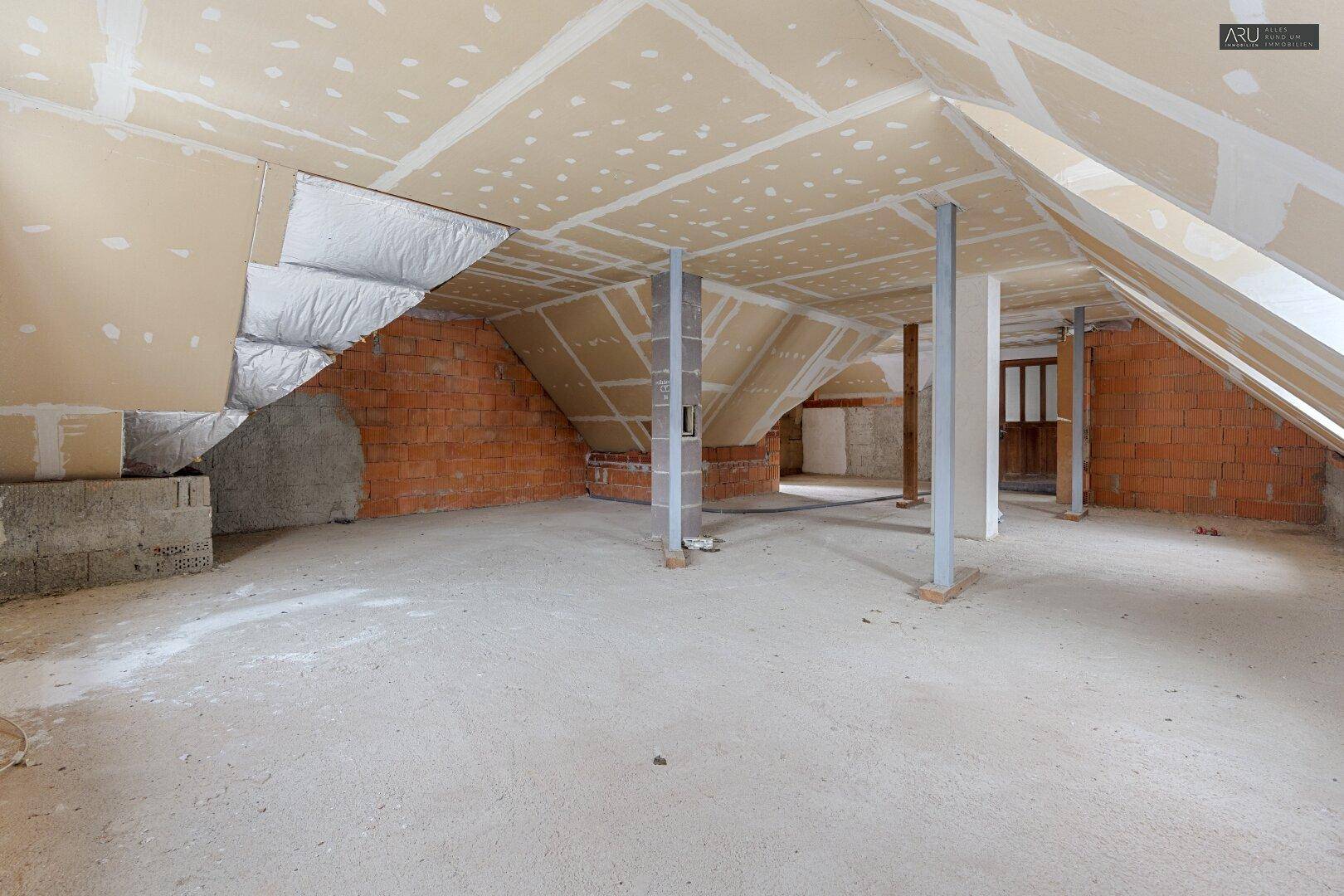Unausgebauter Dachboden mit sichtbaren Dachschrägen, Ziegelwänden und Stützpfeilern, bereit für den Ausbau.