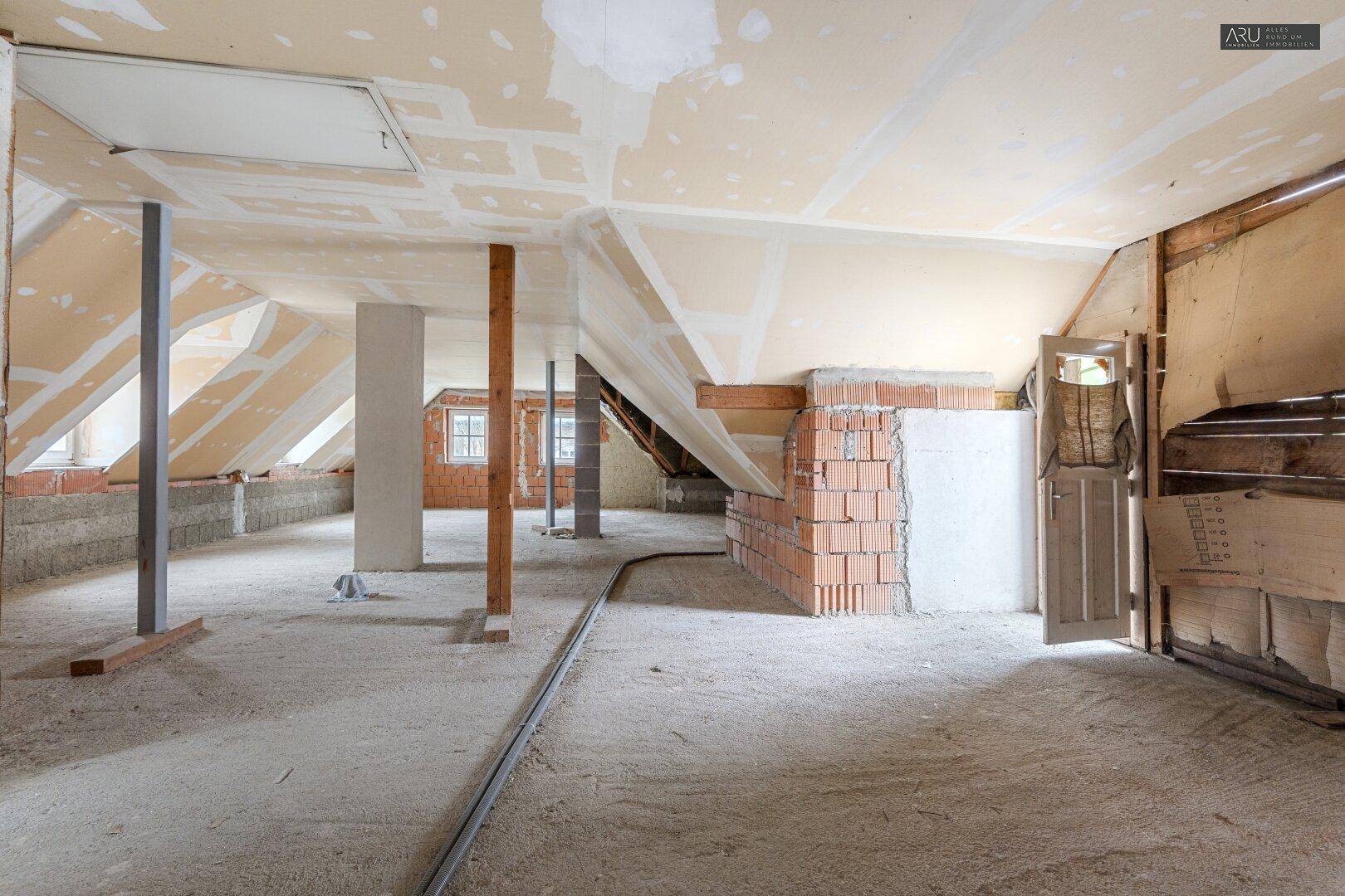 Unausgebauter Dachbodenbereich mit sichtbaren Dachschrägen, Ziegelwänden und Stützpfeilern.