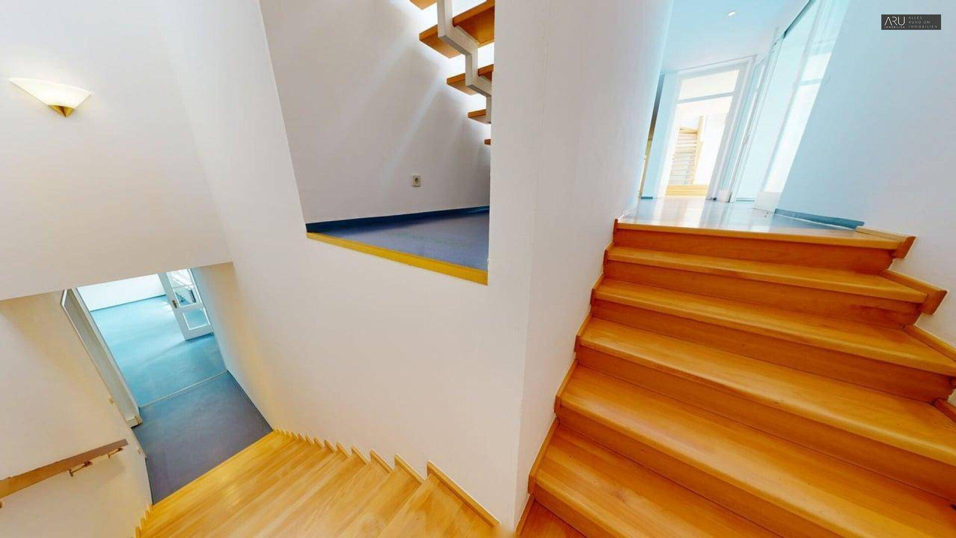 Treppenhaus mit Holzstufen und weiß gestrichenen Wänden, das verschiedene Ebenen verbindet.