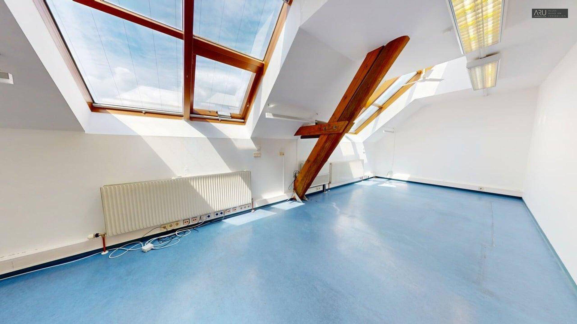 Dachgeschossbüro mit blauer Bodenfläche, großen Dachfenstern und sichtbaren Heizkörpern.
