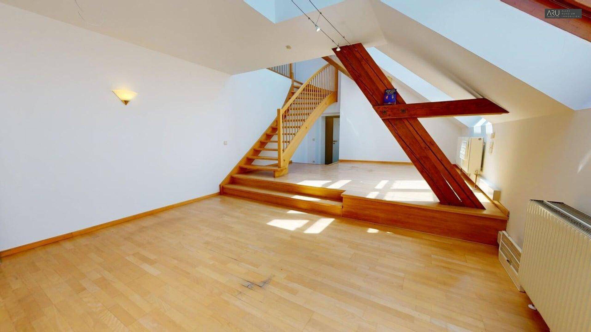 Geräumiges Dachgeschosszimmer mit Holzfußboden, sichtbaren Holzbalken und Treppenaufgang.