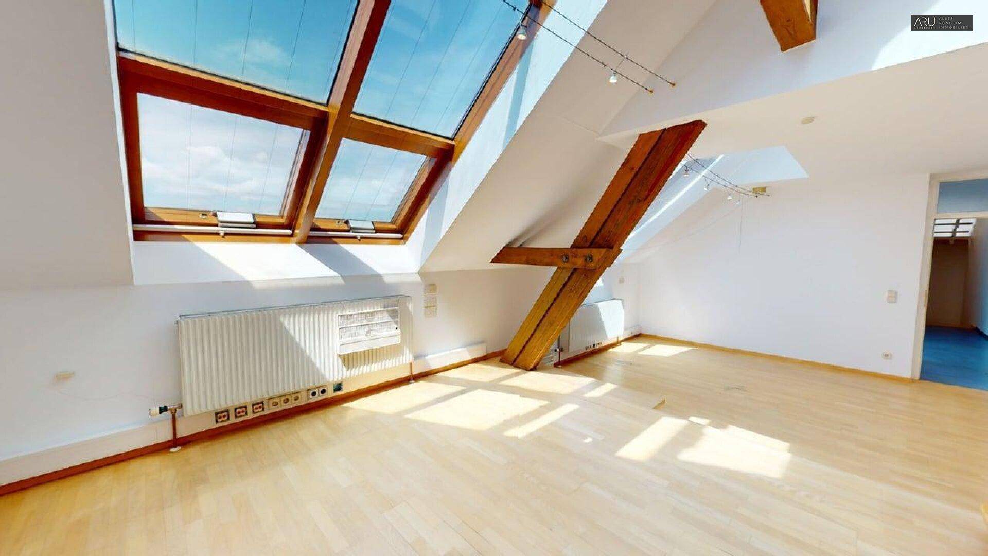 Helles Dachgeschosszimmer mit großen Dachfenstern, Holzbalken und Holzfußboden.