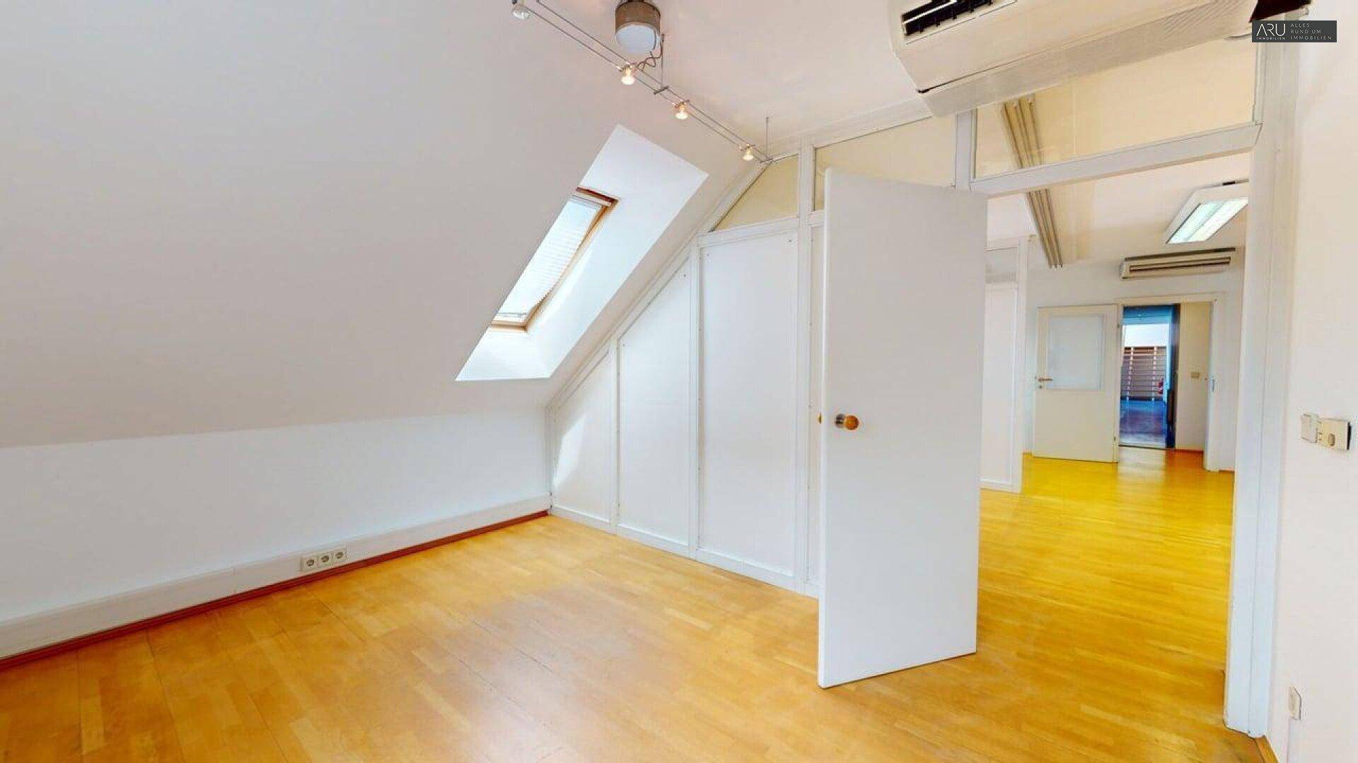 Dachgeschossbüro mit Holzfußboden, Dachfenster und Klimaanlage an der Decke.