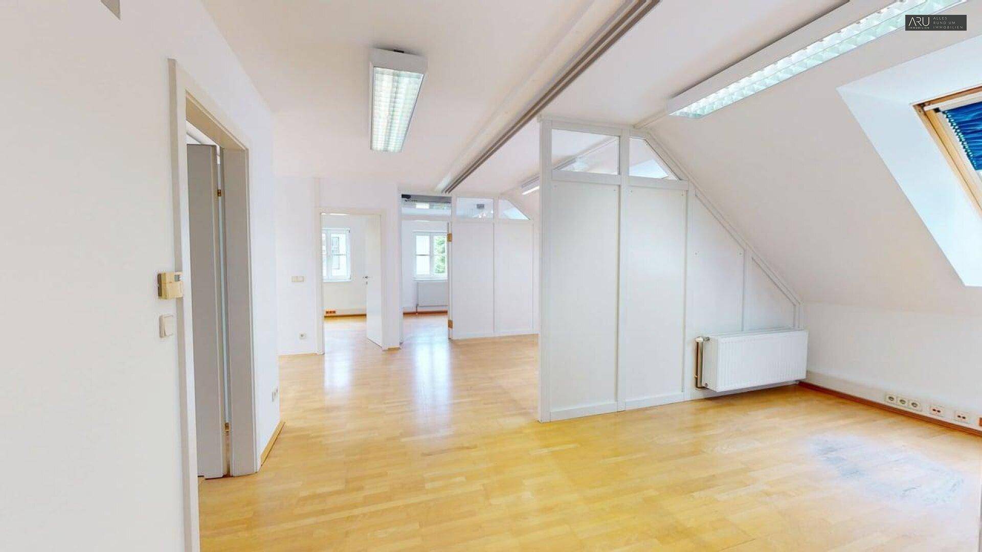 Geräumiges Büro im Dachgeschoss mit Holzfußboden, Dachfenstern und schrägen Wänden.