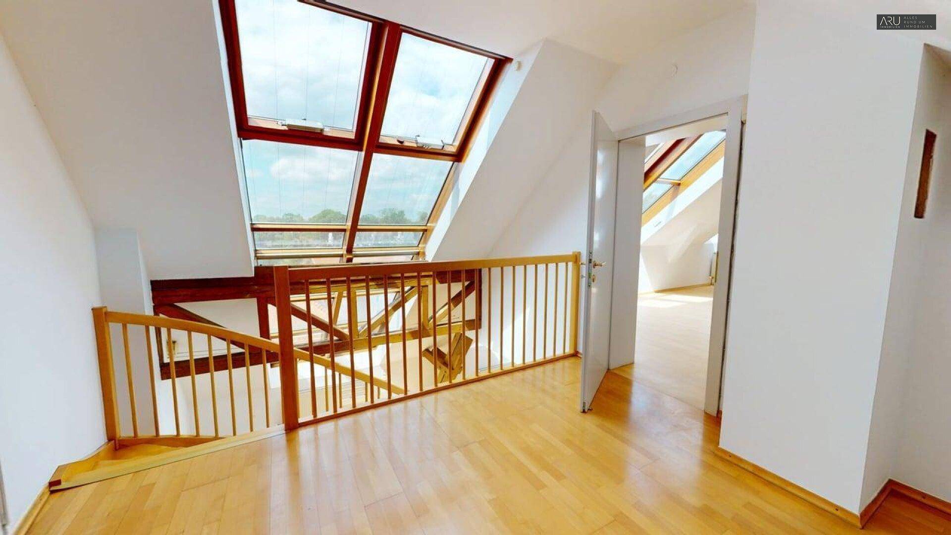 Heller Flur im Dachgeschoss mit Holzfußboden, Geländer und Blick auf Dachfenster.