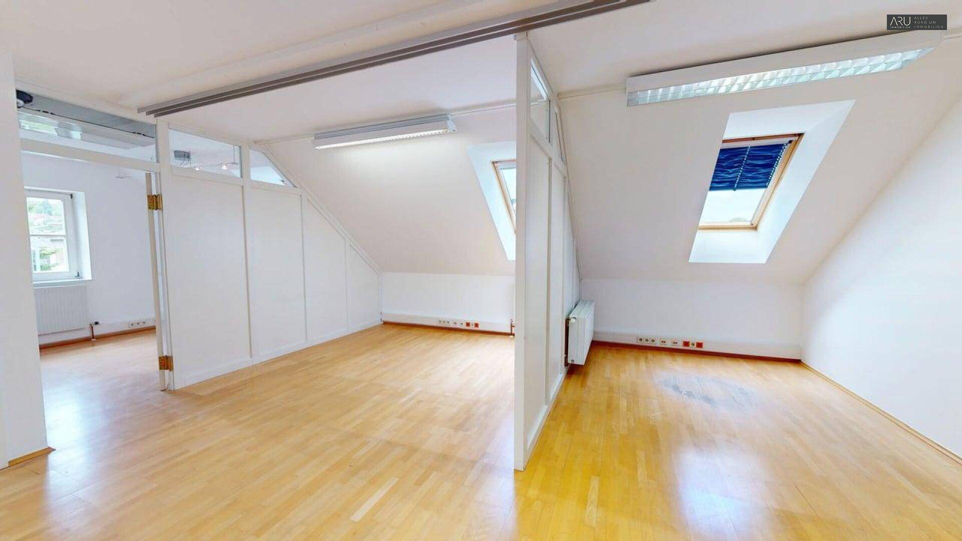 Büro im Dachgeschoss mit hellem Holzfußboden, Dachfenstern und Trennwänden.