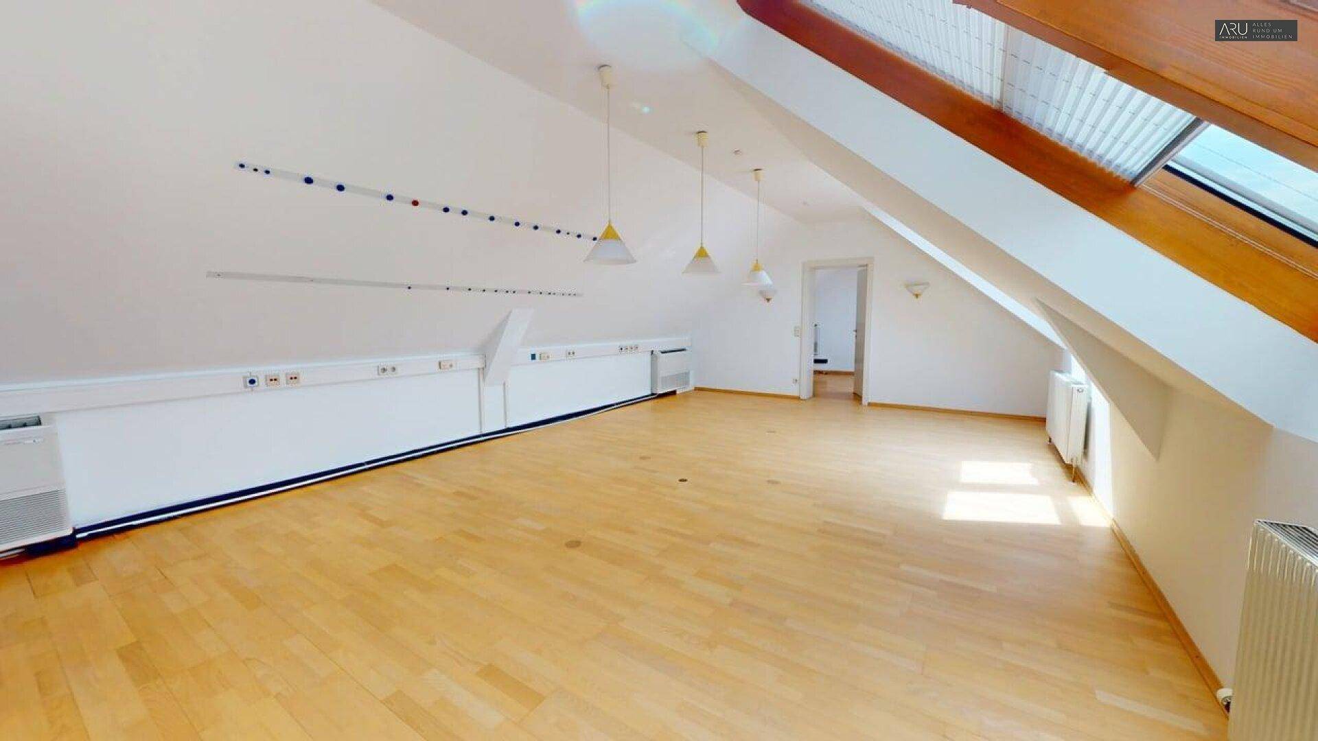 Großes Dachgeschosszimmer mit Holzfußboden, Dachfenstern und schrägen Wänden.