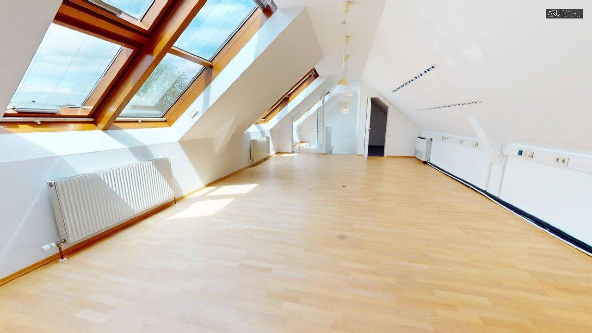 Großes Dachgeschossbüro mit mehreren Dachfenstern, hellem Holzfußboden und viel Tageslicht.