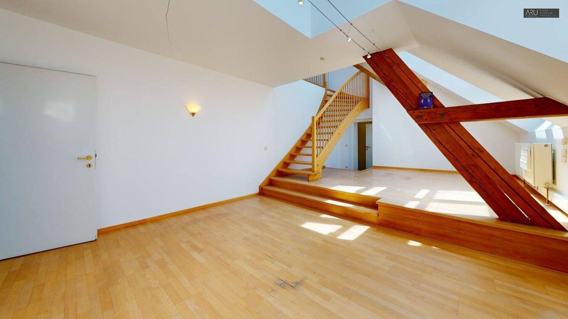Geräumiges Dachgeschosszimmer mit Holzfußboden, sichtbaren Holzbalken und Treppenaufgang.