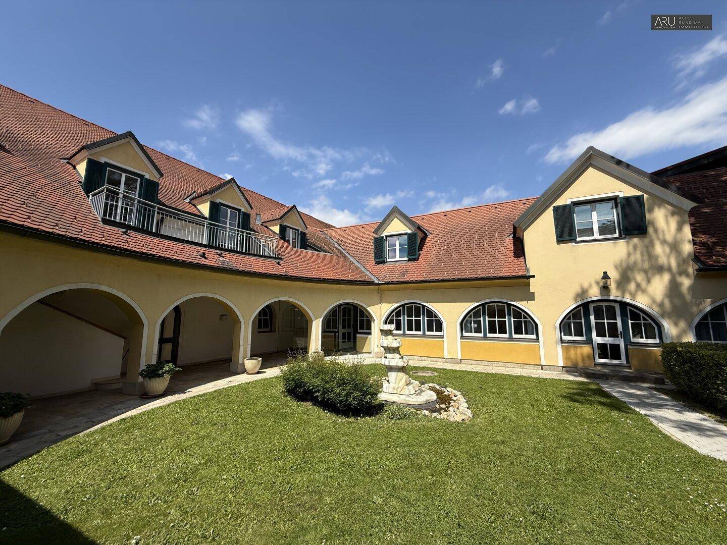 Malerischer Innenhof mit gepflegtem Rasen, einem Brunnen und traditioneller Architektur.