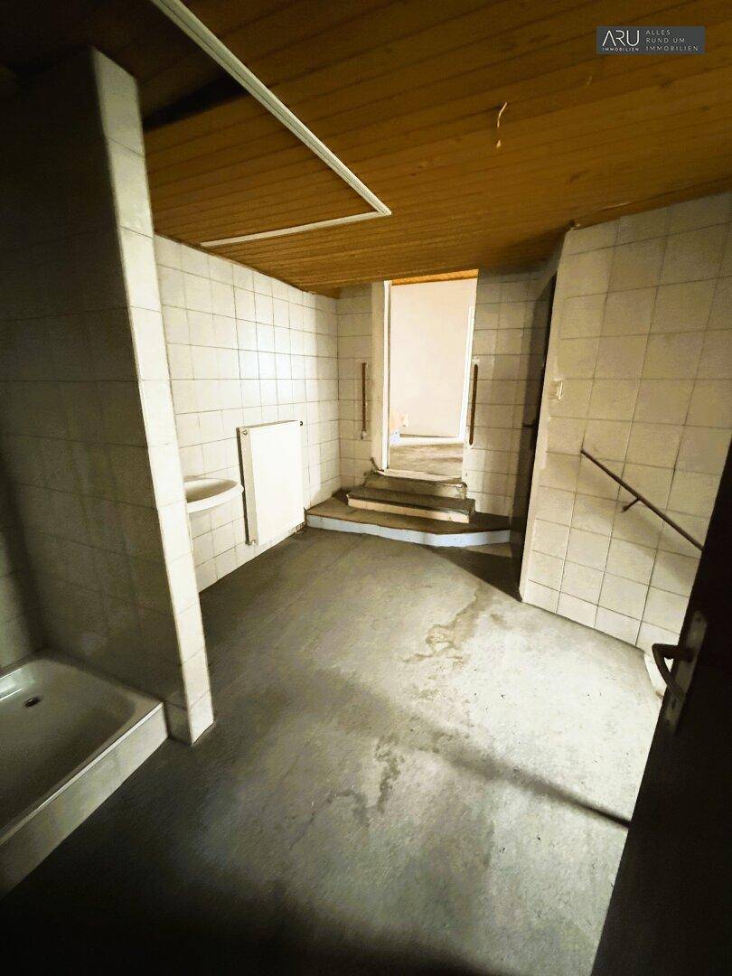Einfacher Badezimmerbereich mit gefliesten Wänden, Duschwanne und Holzdecke, in Renovierungsbedarf.