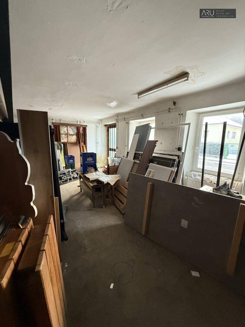 Langer Werkstattraum mit Fenstern, Betonboden und gelagerten Materialien.