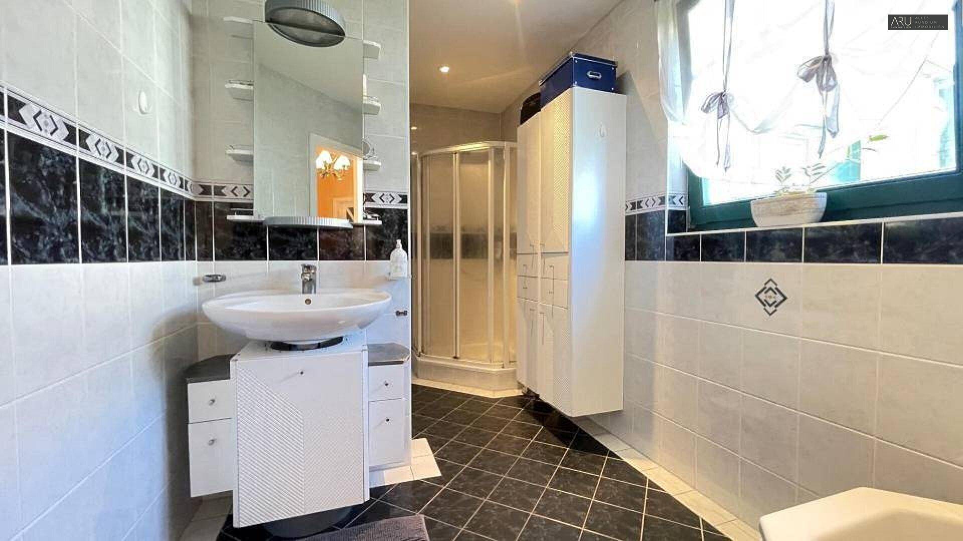 Modern gefliestes Badezimmer mit Dusche, Waschbecken und Fenster für Tageslicht.