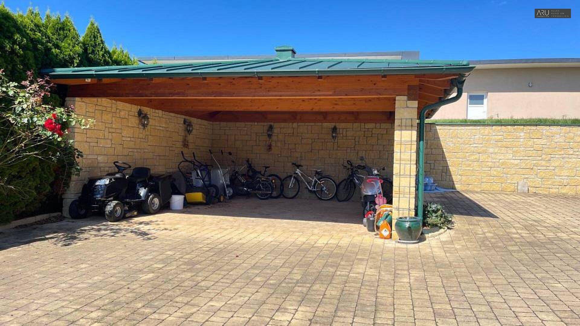 Überdachter Carport mit Holzbalken und Stauraum für Fahrräder und Gartengeräte.