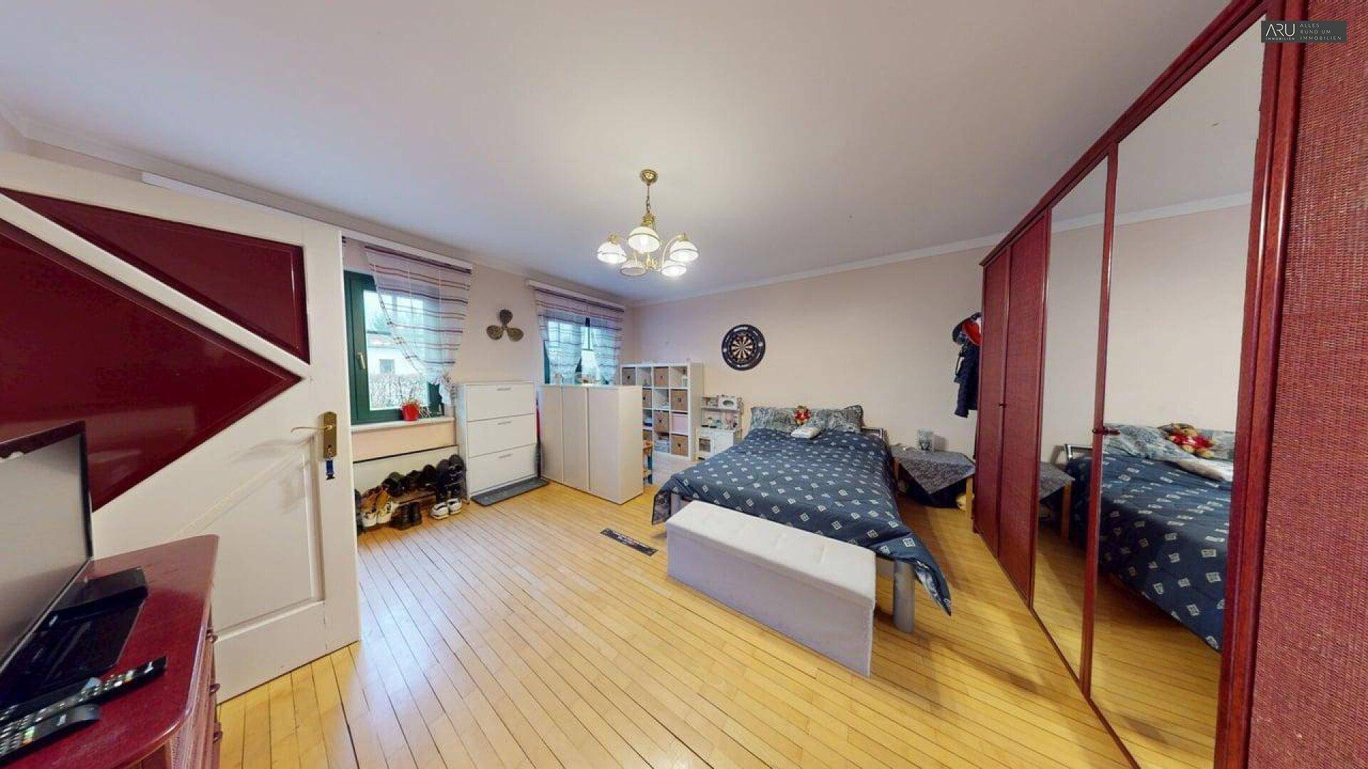 Geräumiges Schlafzimmer mit Holzparkett, großem Spiegelschrank und Fensterblick.