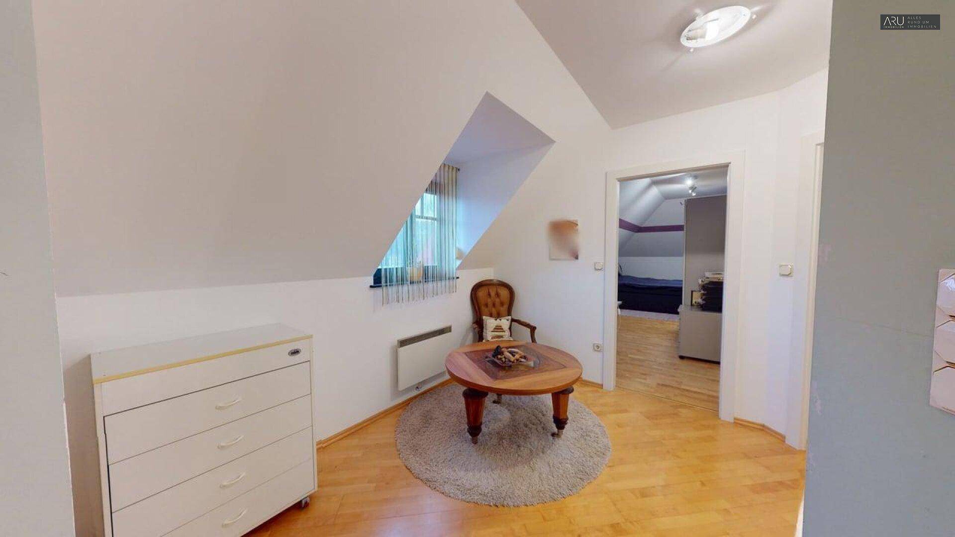 Gemütlicher Dachraum mit schrägen Wänden, Holzboden und kleinem Fenster.