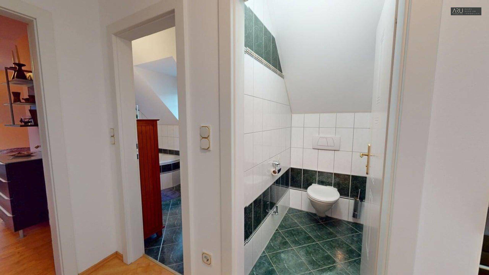 Kleines Gäste-WC mit Wand-WC und Fliesen in Schwarz-Weiß-Grün.