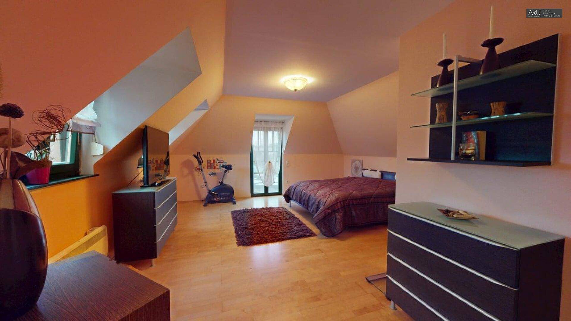 Geräumiges Schlafzimmer im Dachgeschoss mit Holzboden, Dachschrägen und Zugang zu einem kleinen Balkon.