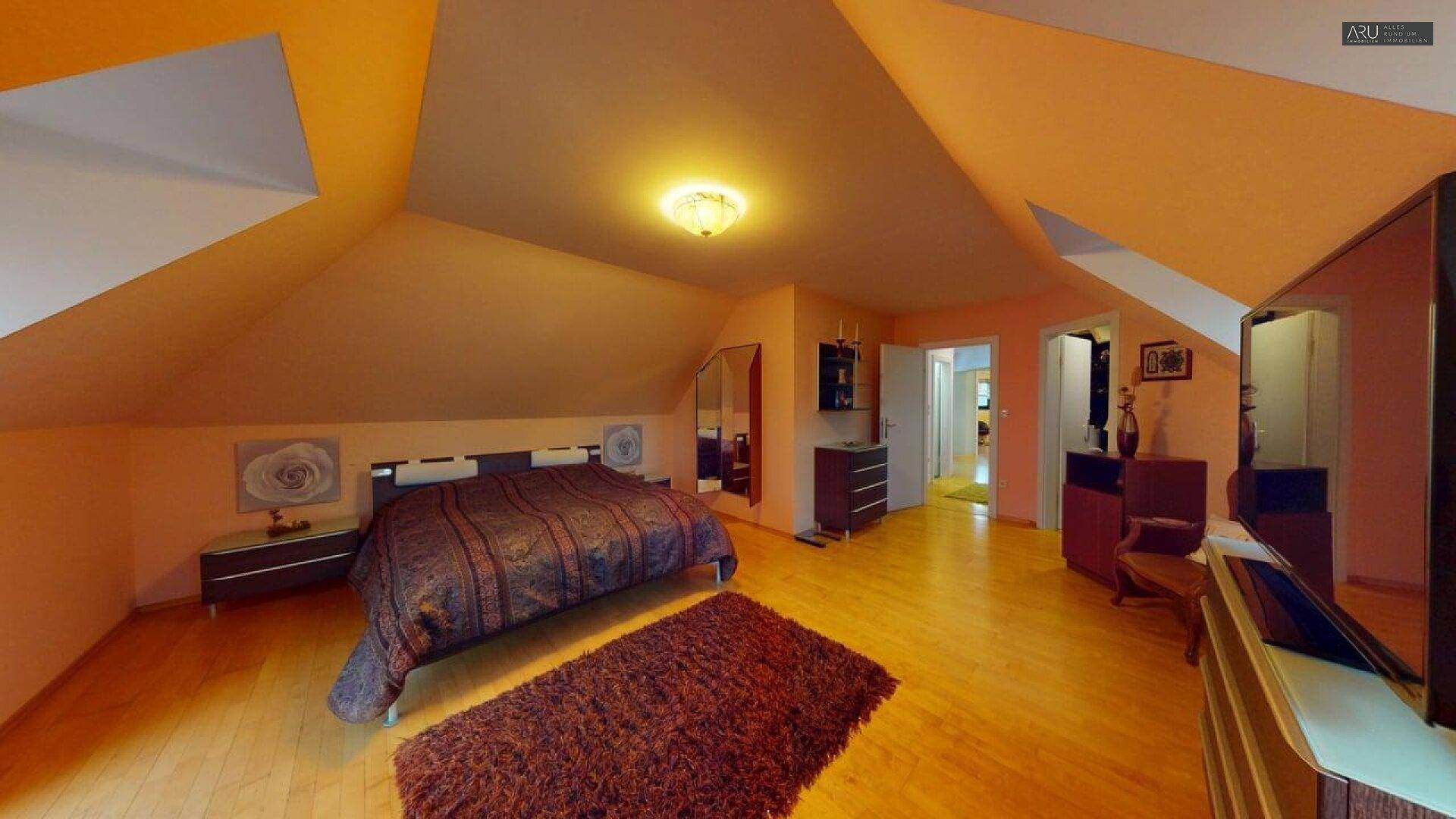 Helles Schlafzimmer mit Holzboden, Dachschrägen und einem großen Bett.