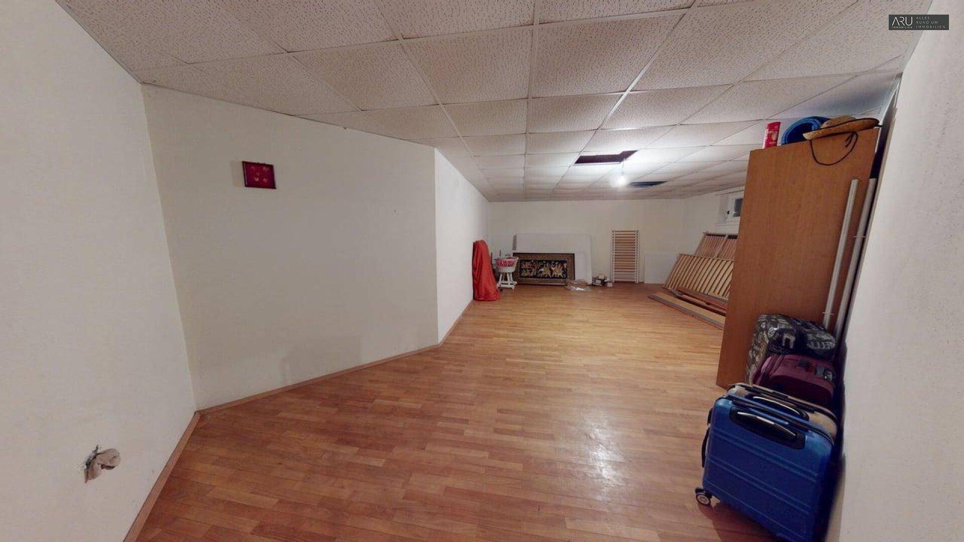 Heller Kellerraum mit Holzboden und einem gemauerten Kamin im Hintergrund.