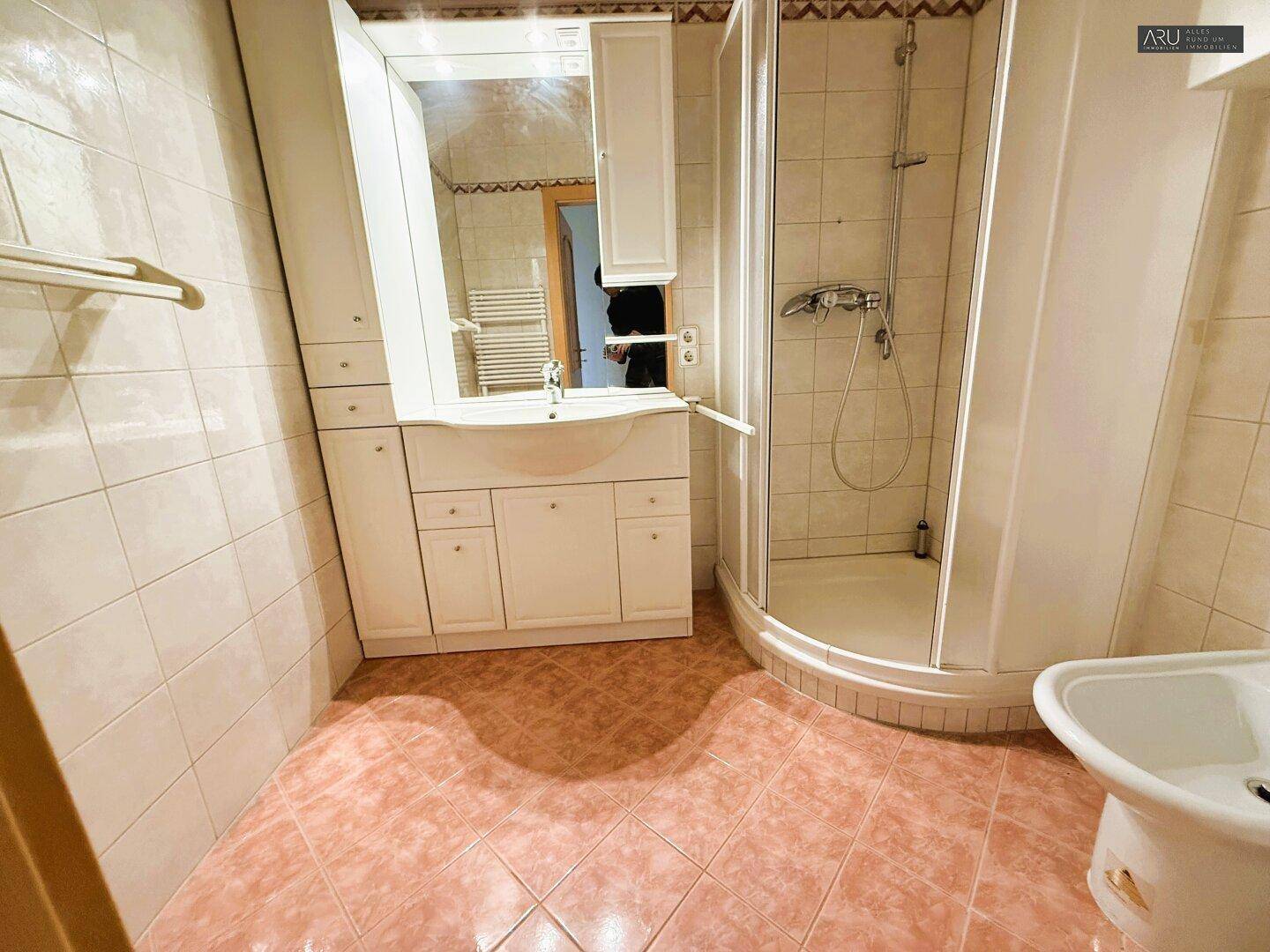 Badezimmer mit Dusche, Waschbecken und Bidet, gefliest in Rosa- und Weißtönen.