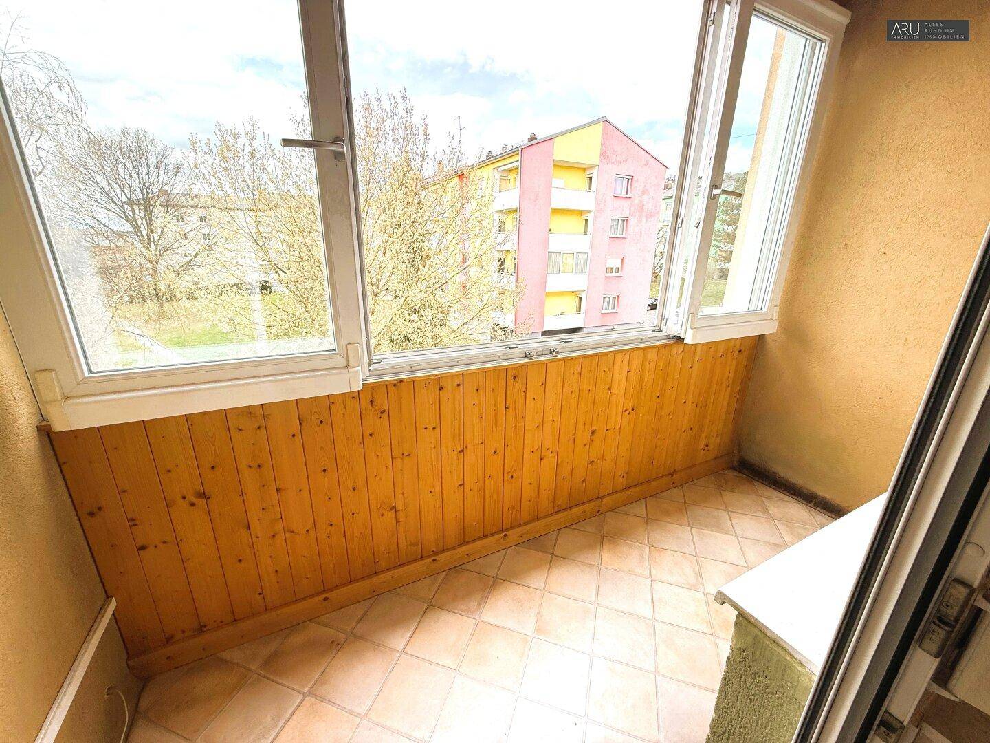 Verglaster Balkon mit Holzverkleidung und Fliesenboden, bietet zusätzlichen Wohnraum.