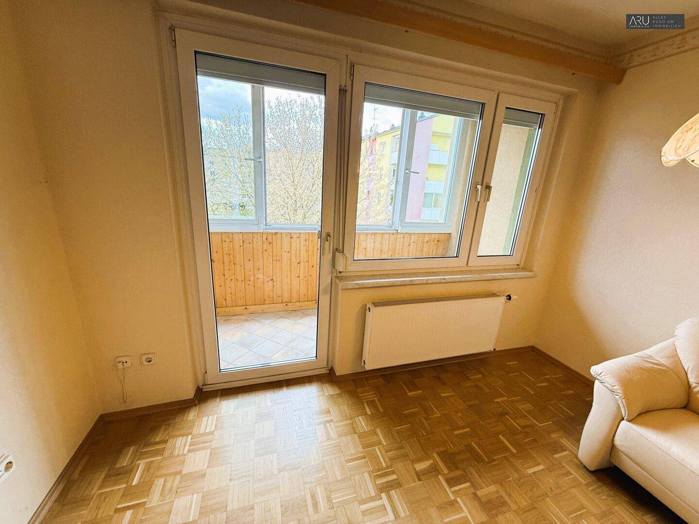 Wohnzimmer mit Parkettboden und Zugang zu einem verglasten Balkon.