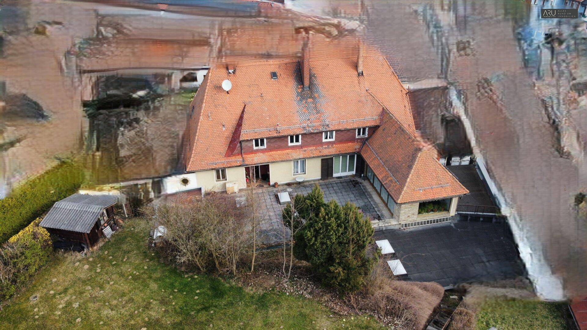 Luftaufnahme des Hauses mit großer Terrasse und umliegendem Gartenbereich, leicht digital bearbeitet.