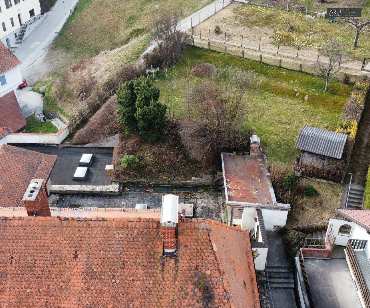 Blick von oben auf das Grundstück mit Garten, Nebengebäuden und angrenzenden Grünflächen.