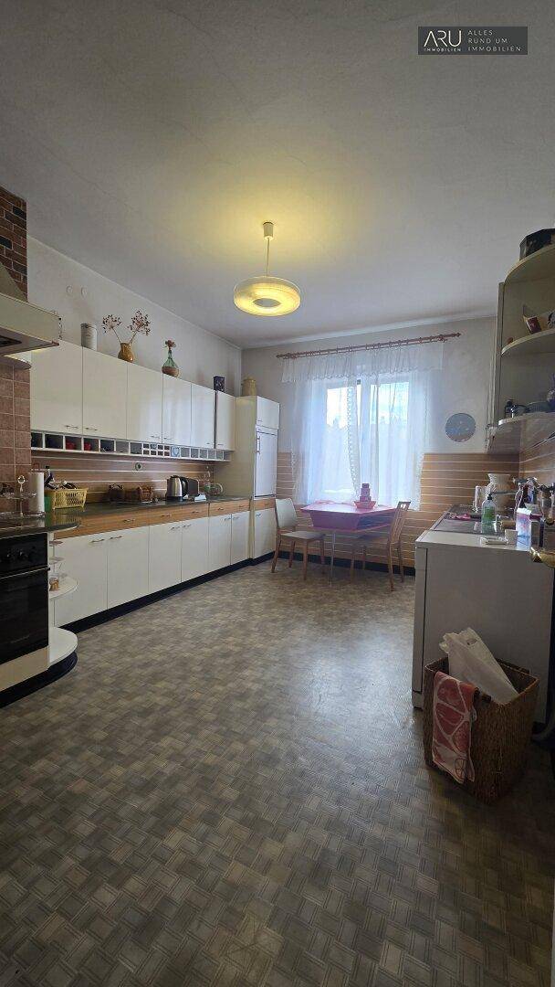 Geräumige Küche mit weißen Schränken, einem Essbereich am Fenster und gemusterten Fliesenboden.
