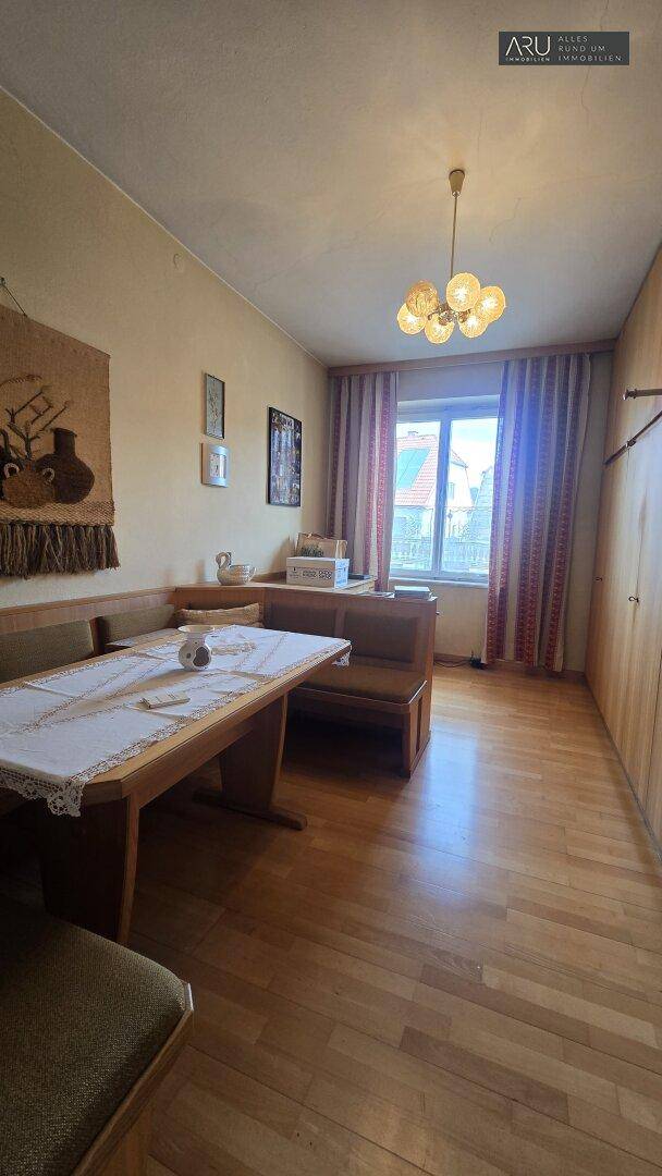 Gemütliches Esszimmer mit Holzbänken, einem Esstisch und Holzparkettboden, hell durch das Fenster.