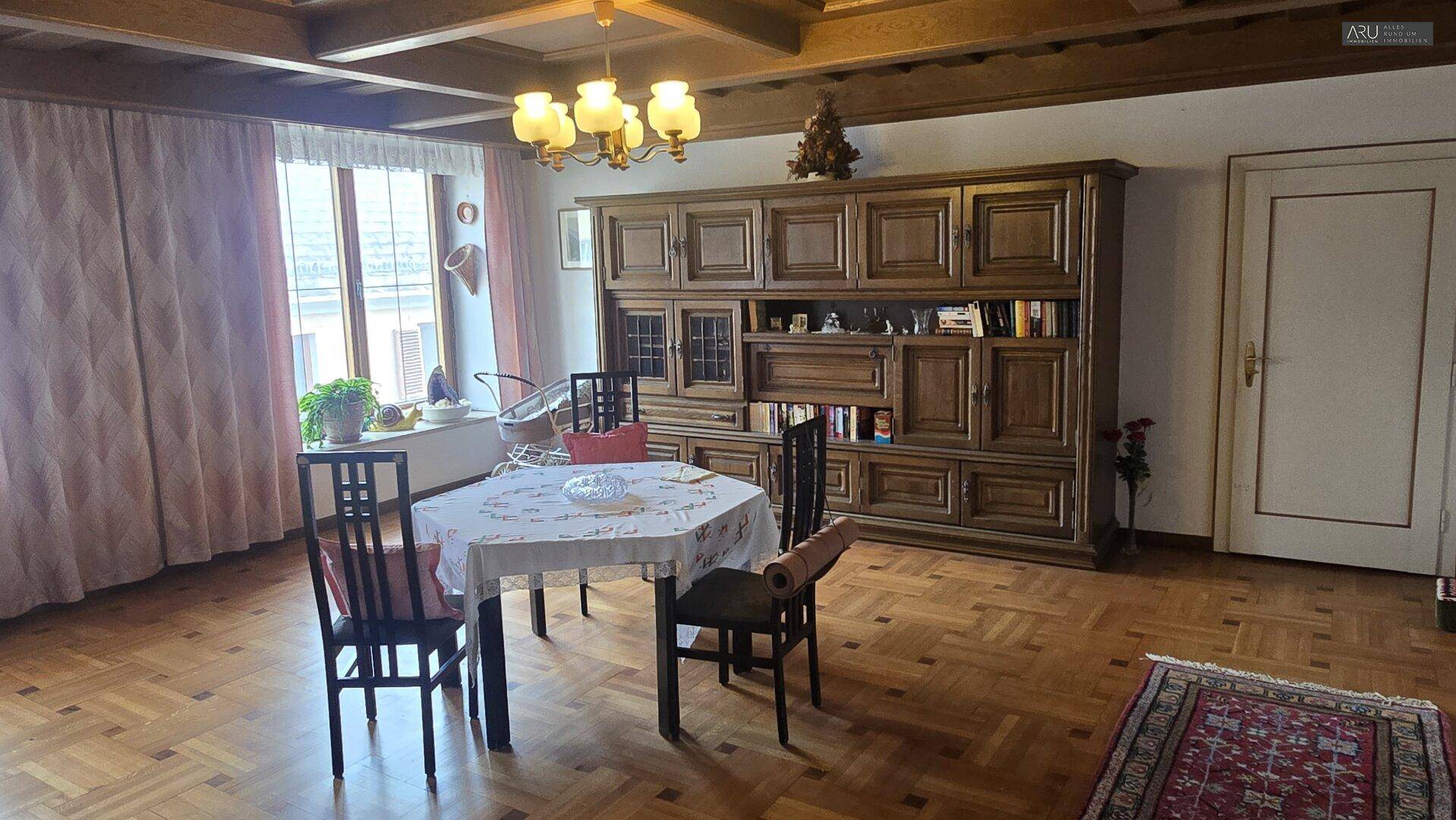 Wohn-Essbereich mit Parkettboden, großer Holzschrankwand und Esstisch unter Holzbalkendecke.