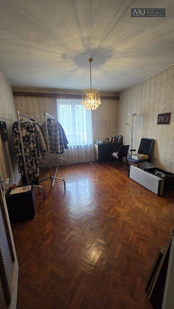 Schlafzimmer oder Mehrzweckraum mit Fischgrätparkett, Fenster und einem Kleiderständer.