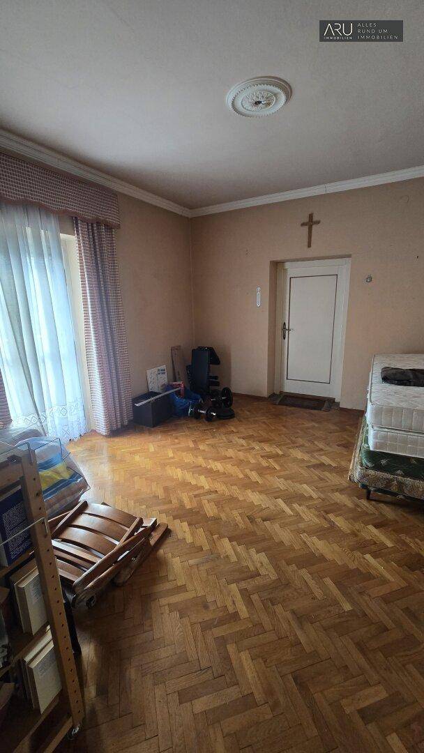 Helles Schlafzimmer mit Fischgrätparkettboden und einem großen Fenster, das viel Licht hereinlässt.