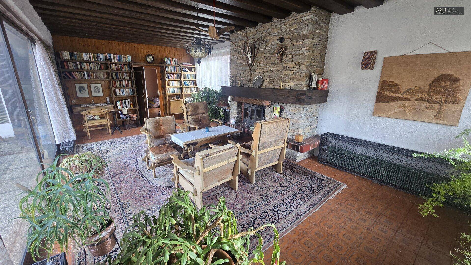 Geräumiges Wohnzimmer mit Steinkamin, Bücherregalen, traditionellen Möbeln und Terracotta-Fliesenboden.
