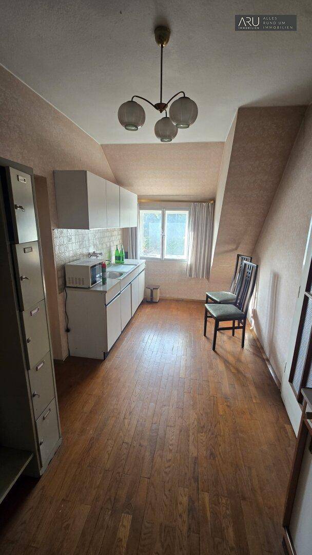 Kleine Küche im Dachgeschoss mit Holzboden, Dachschrägen und einem Fenster für Tageslicht.