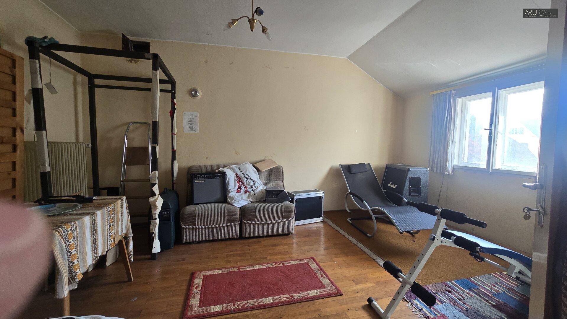 Vielseitiger Wohnraum im Dachgeschoss mit Holzboden, Sofa und Fitnessgeräten unter der Dachschräge.