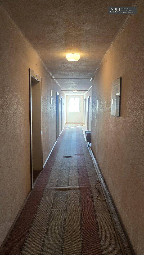 Heller, langer Flur mit gemustertem Teppichläufer und einem Fenster am Ende für natürliches Licht.