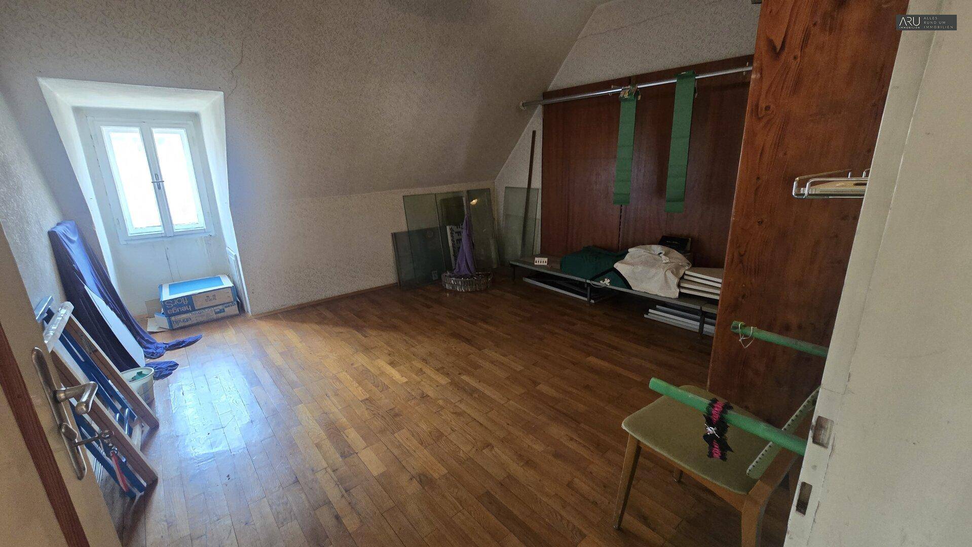 Geräumiger Dachbodenraum mit Holzboden, Dachschrägen und einem Fenster, ideal als Abstellraum.