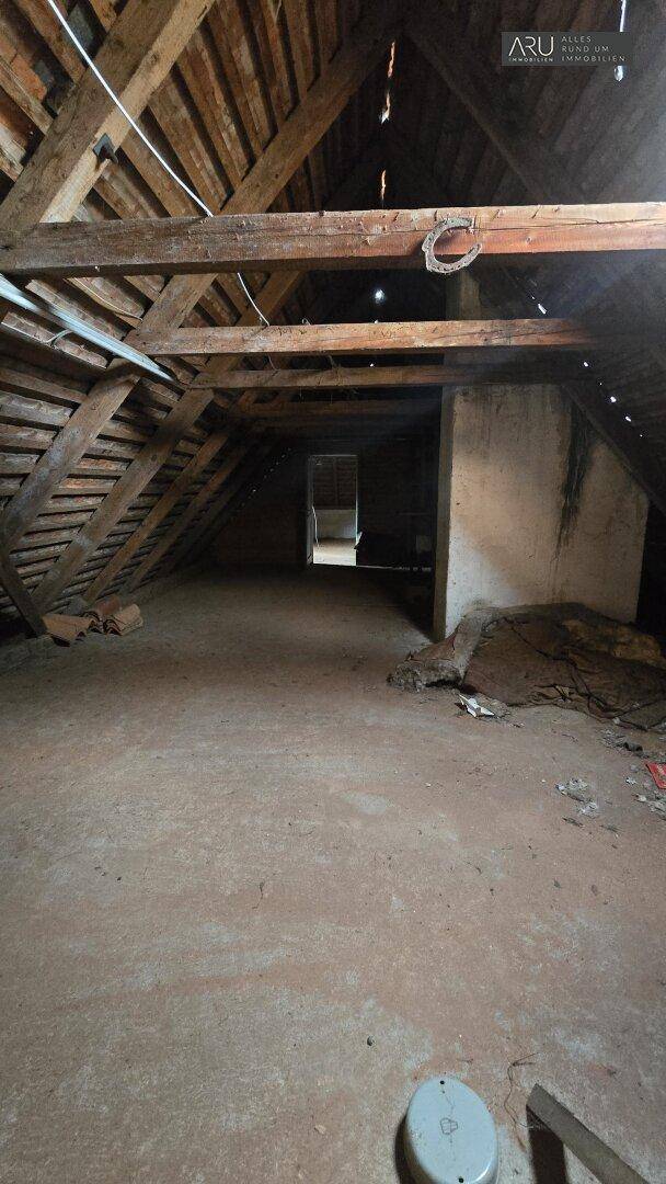 Unausgebauter Dachboden mit sichtbaren Holzbalken und Betonboden, ideal für zukünftige Nutzung.