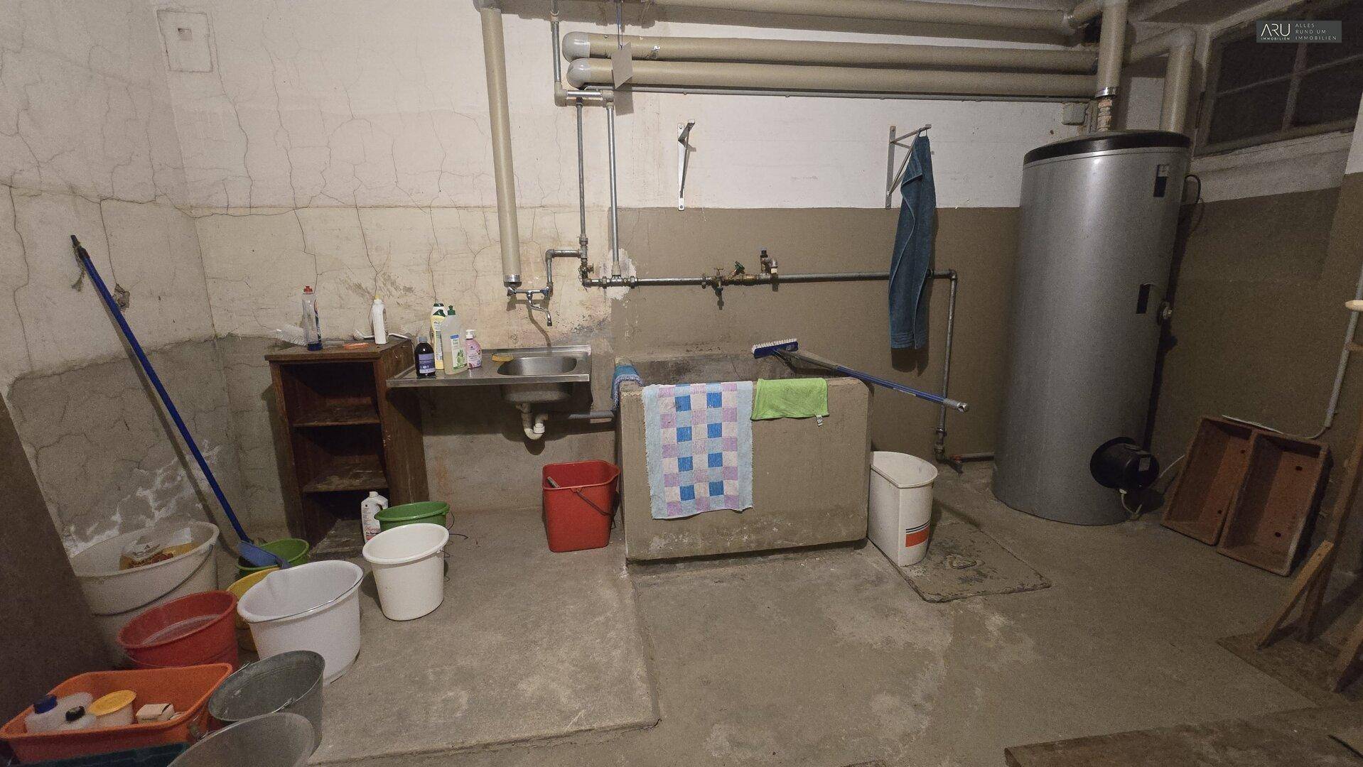 Hauswirtschaftsraum im Keller mit Warmwasserbereiter, Waschbecken und Reinigungsutensilien.