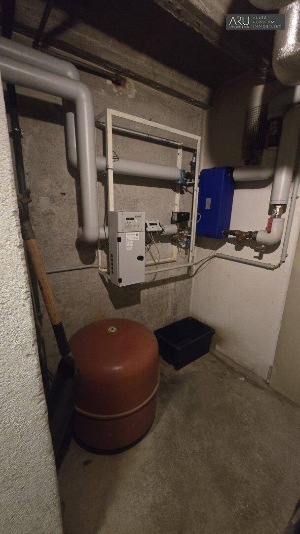 Technischer Raum im Keller mit Rohrleitungen, Steuerung und einem Ausdehnungsgefäß.